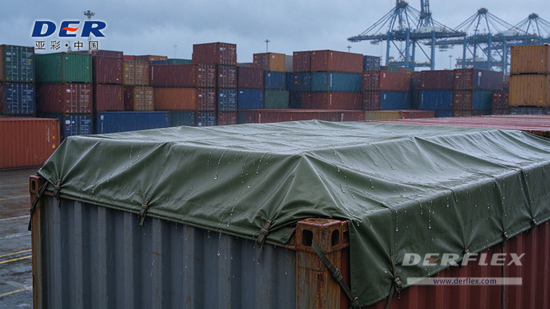Green PVC container tarp covering the top and edges of an open-top shipping container in a wet container yard