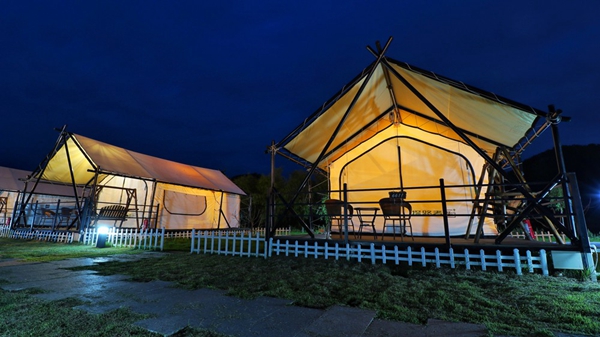 Hospitality tents illuminated at night showing light passing through yellow outer roof canopies