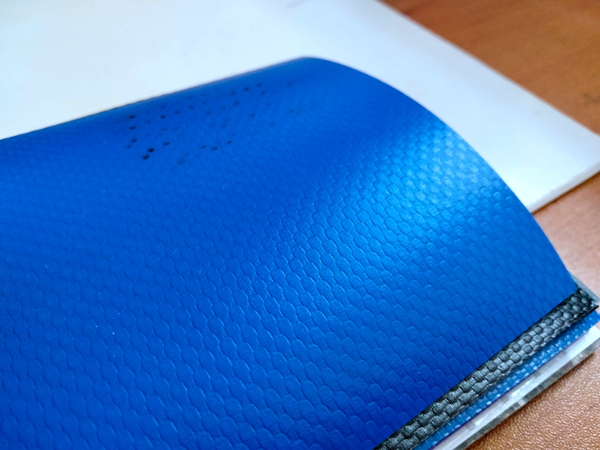 Close view of a blue PVC coated woven fabric sample showing the surface texture and cut edge